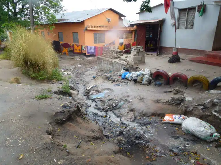 Small river channel running through colourful settlement in the Msimbazi River Basin, Tanzania. Depicting everyday life with washing hanging on the line. Tires and sandbags line the banks of the channel.