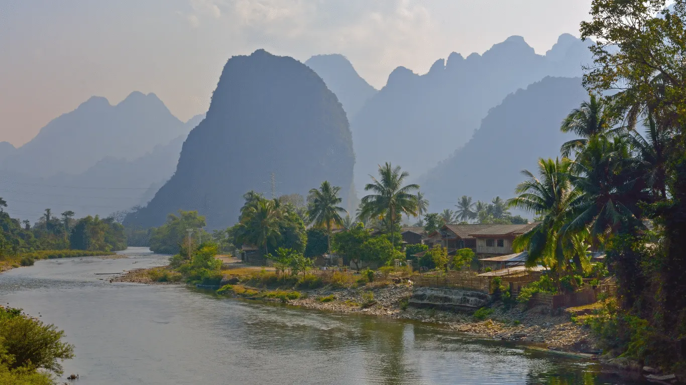 Rural scene of a river and settlement in the forefround and mountain range in the background. Lao PDR.