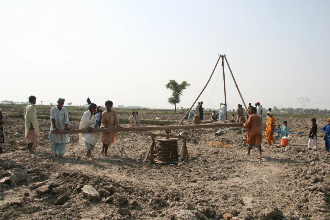 Men, women and children working and watching borehole drilling for a temporary water supply, Pakistan.
