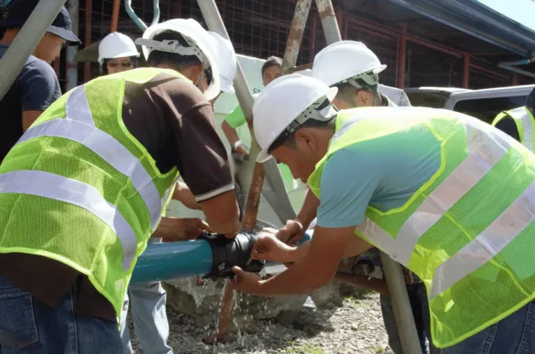 People wearing hard hats and high vis jackets, gathered around and working on a water pipe.