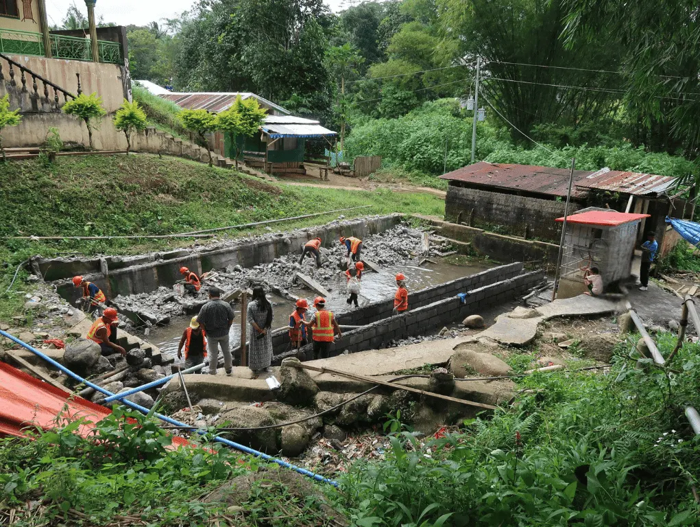 Construction workers building a water and sanitation facility, surrounded by lush tropical vegetation.