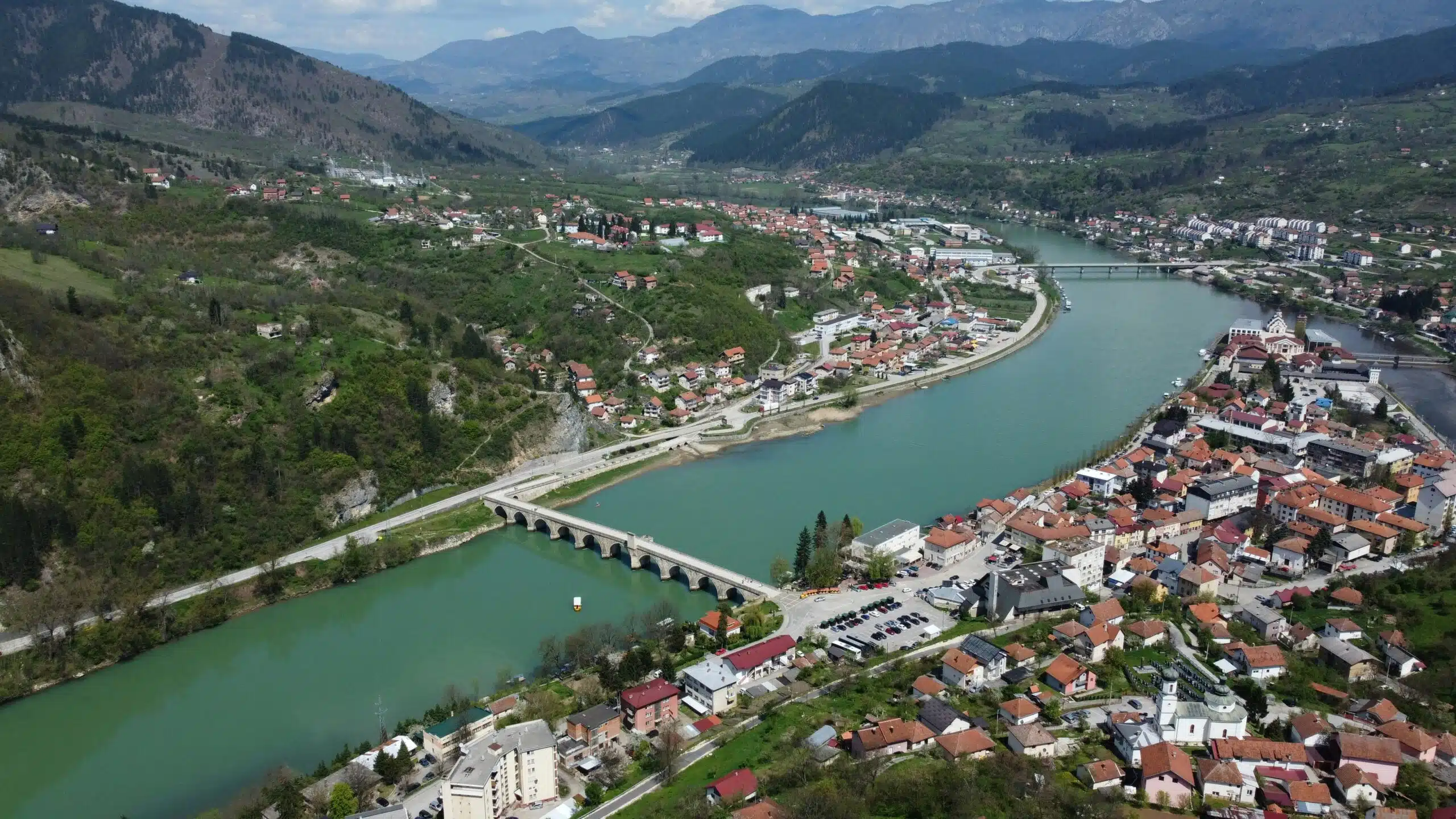 Arial view of wide meandering river with a bridge crossing. With sloping mountains to one side and an urban area to the other.