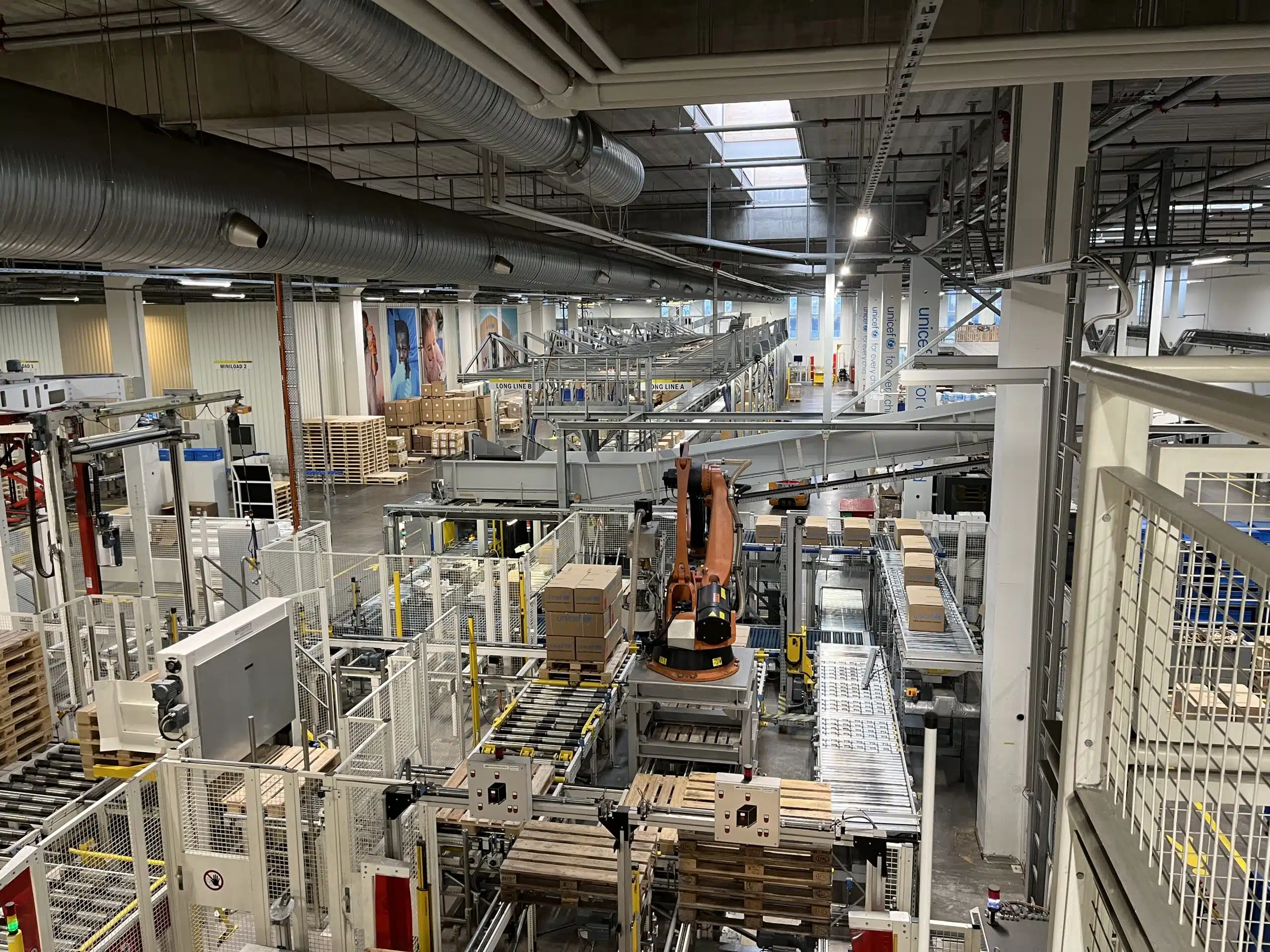 Automated warehouse with robotic arms and conveyor belts handling humanitarian aid packages, showing industrial-scale logistics operations.