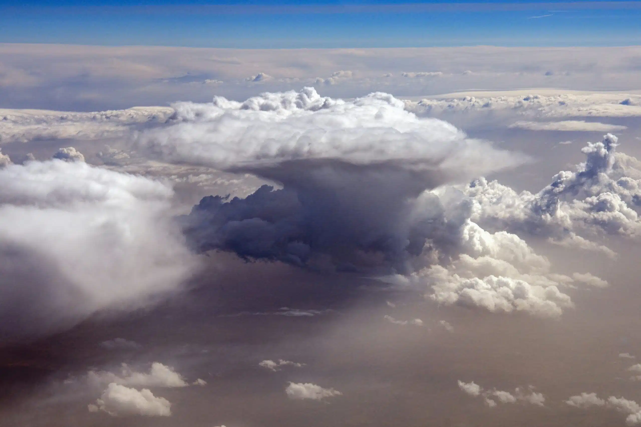 Arial view of large, white convection clouds forming with clouds below and bright blue sky in the background.