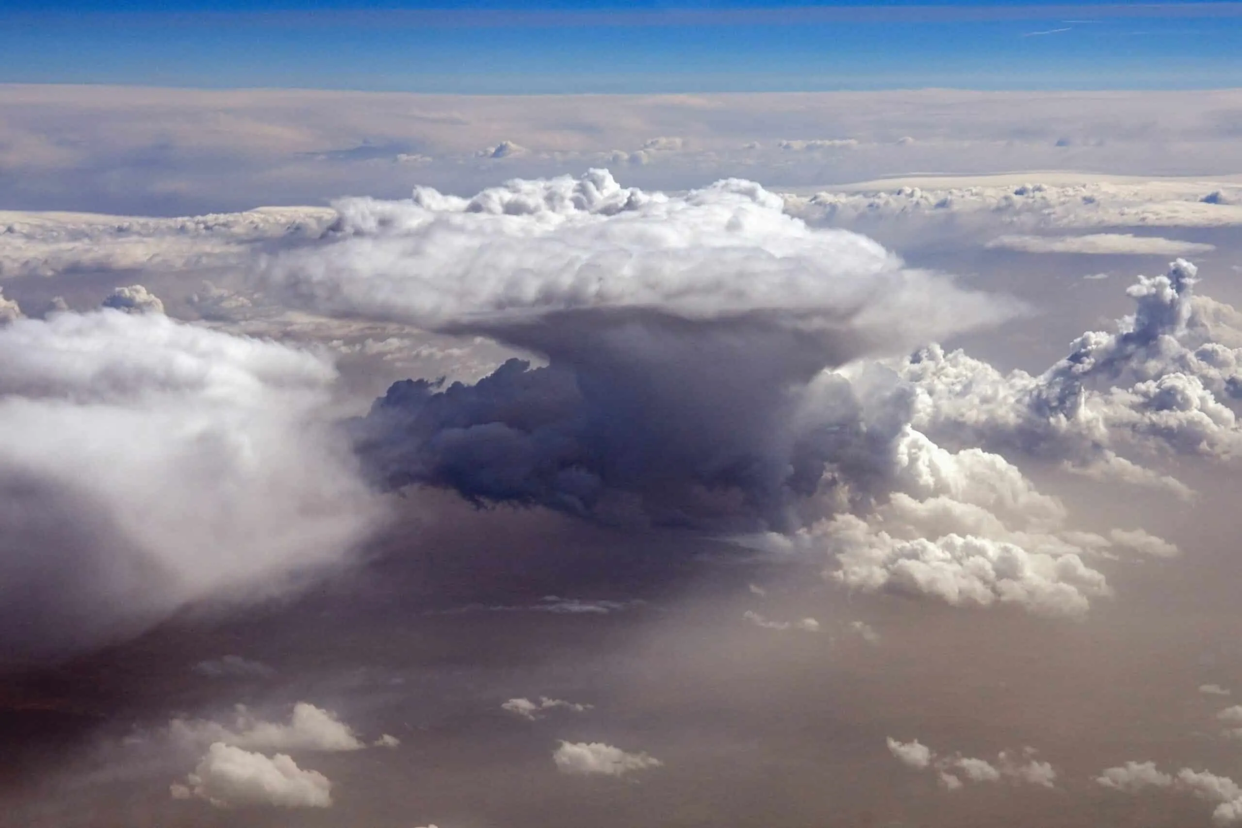 Arial view of large, white convection clouds forming with clouds below and bright blue sky in the background.