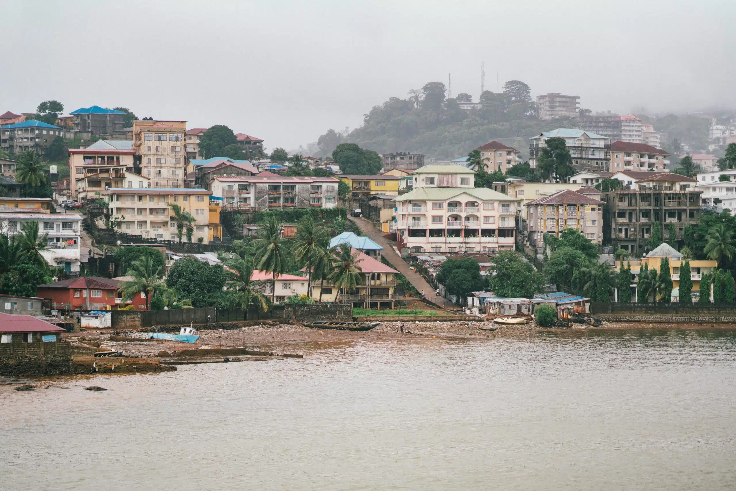 Hillside view of Freetown, Sierra Leone, with waterfront buildings during heavy rainfall, highlighting urban flood risk in West Africa.