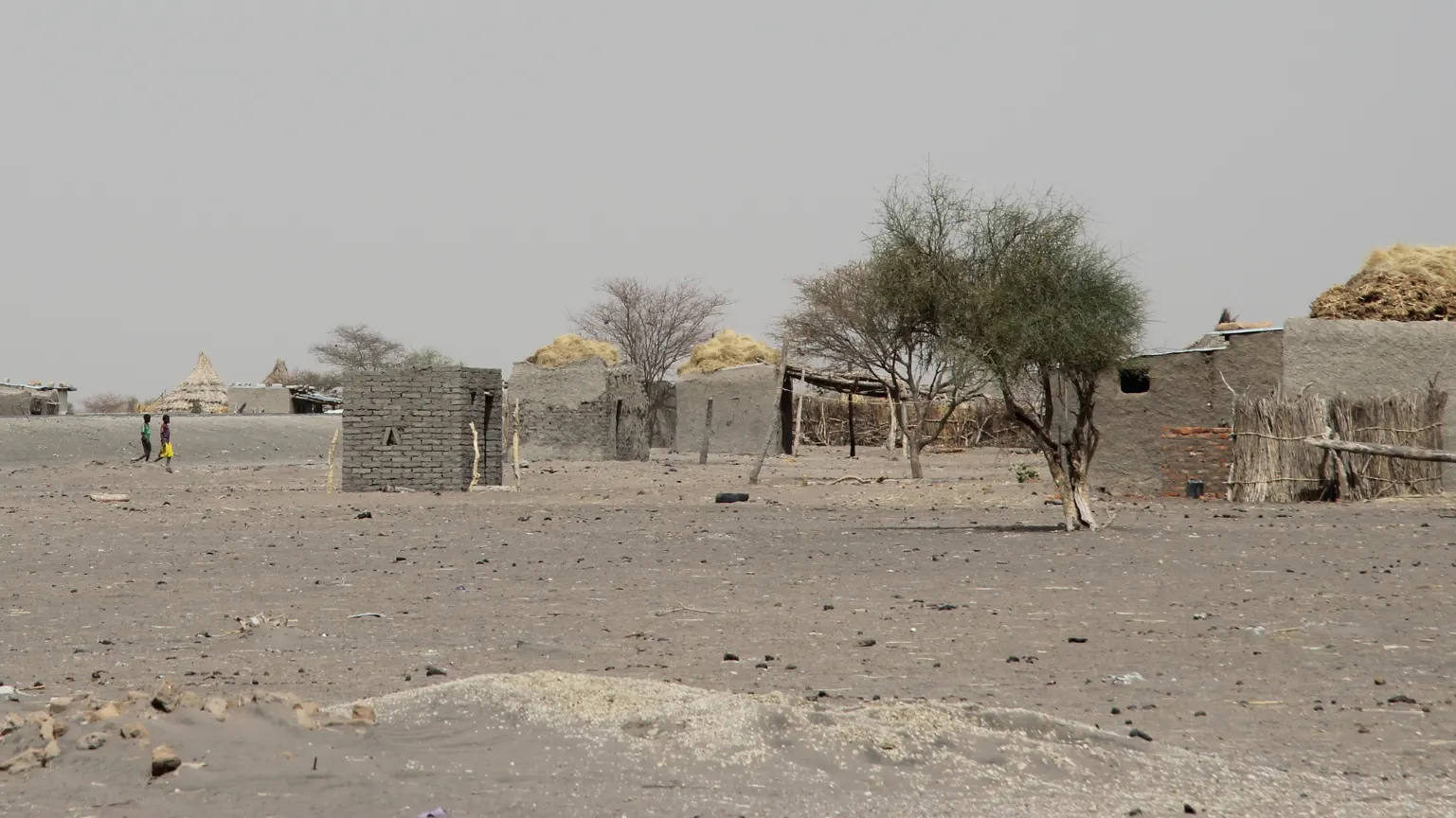 Rural settlement in a dry landscape in Chad, with small buildings and people visible in the distance.