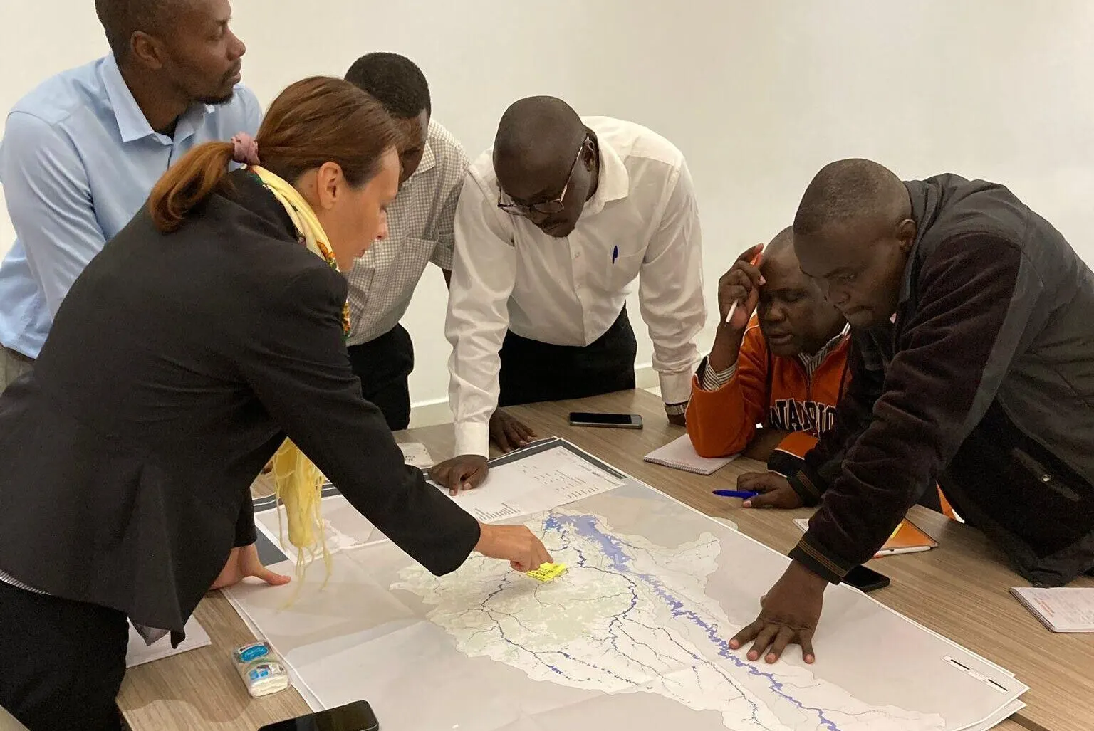 Group of participants gathered around a table reviewing a large printed flood hazard map during a workshop discussion.