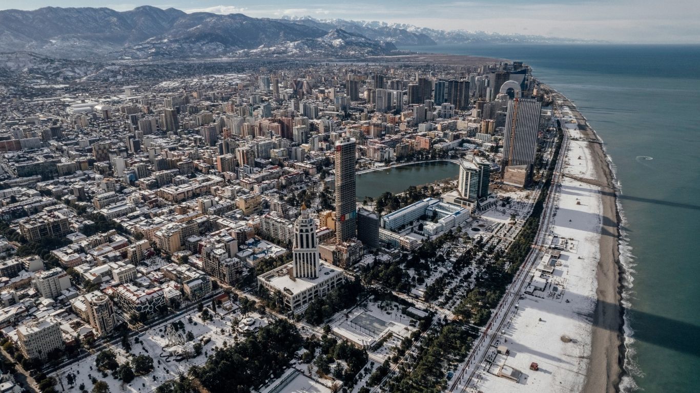Aerial view of a dense coastal city with beachfront, urban buildings, and surrounding mountains.