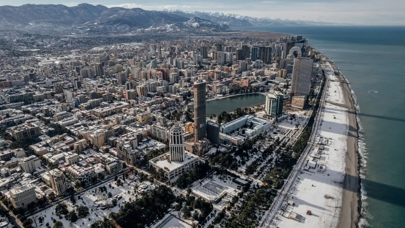 Aerial view of a dense coastal city with beachfront, urban buildings, and surrounding mountains.