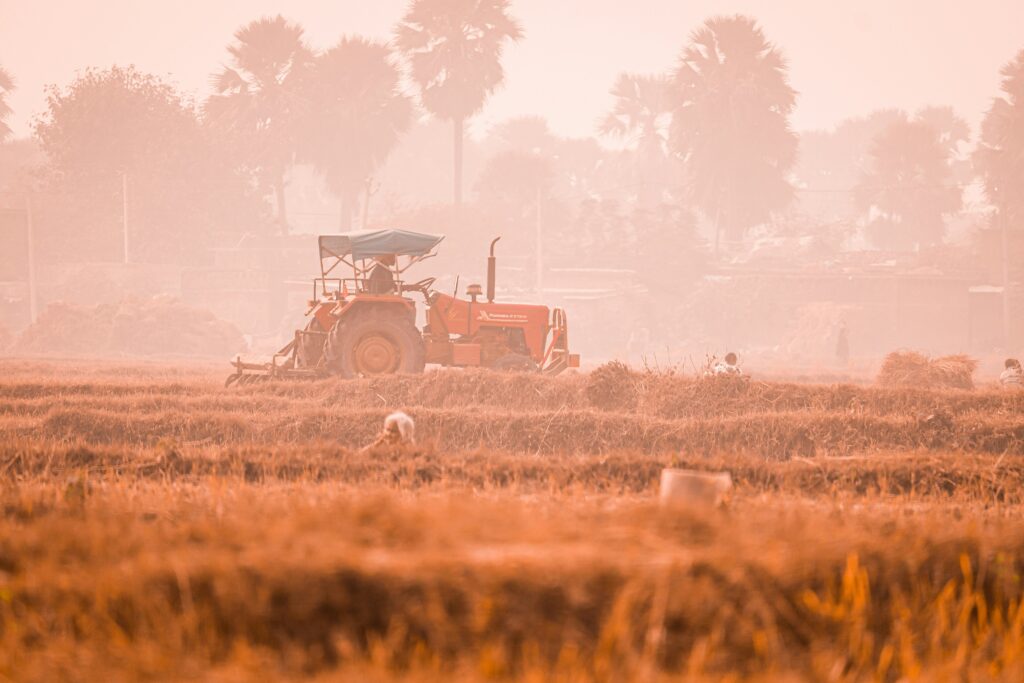 Tractor working in a dry agricultural field with visible dust in the air, illustrating farming conditions under heat and low rainfall
