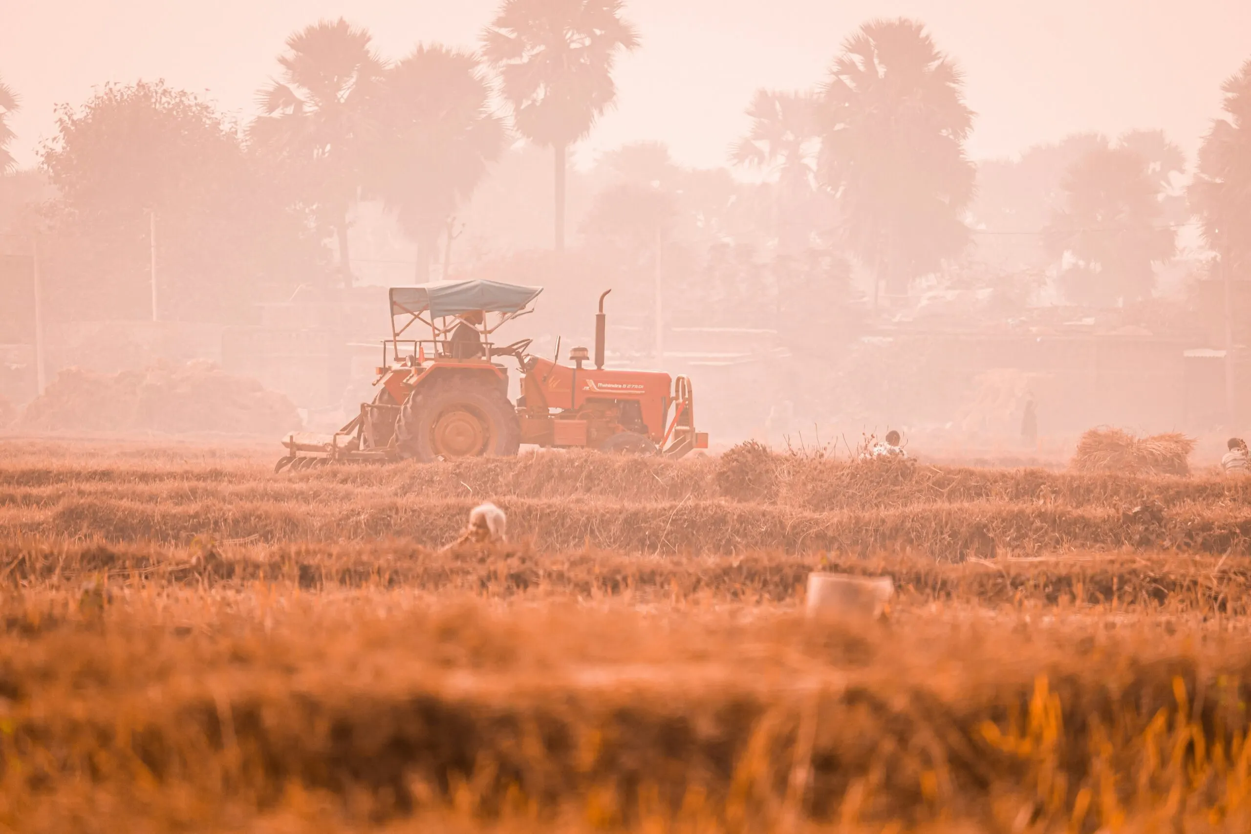 Tractor working in a dry agricultural field with visible dust in the air, illustrating farming conditions under heat and low rainfall