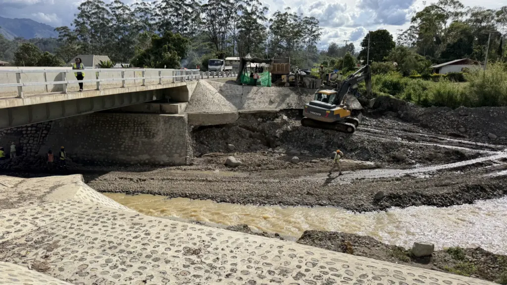 Bridge construction work over a river in Papua New Guinea, with excavators and workers on site beside the bridge structure.